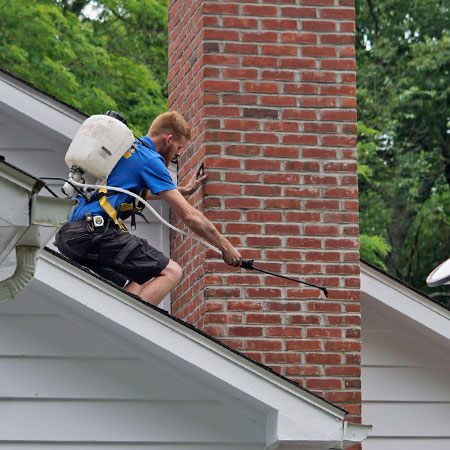 A brick chimney with a metal cap sits on a pitched roof covered in snow - Contact us.