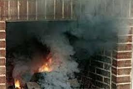 A brick chimney with a metal cap sits on a pitched roof covered in snow - Contact us.