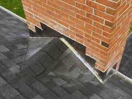 A brick chimney with a metal cap sits on a pitched roof covered in snow - Contact us.