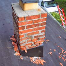 A brick chimney with a metal cap sits on a pitched roof covered in snow - Contact us.
